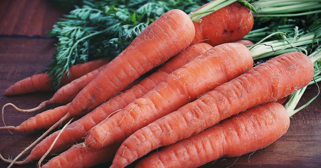 Close-up of fresh organic carrots with greens on a wooden surface, showcasing vibrant orange color.