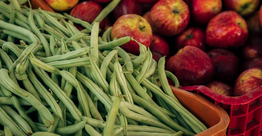 Close-up of fresh green beans and red apples at a local market.