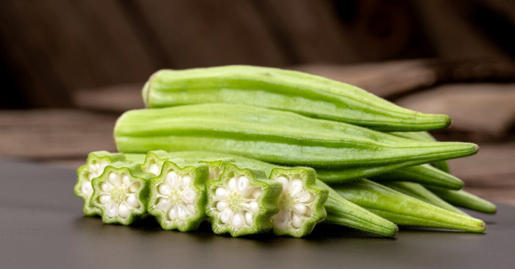 Close-up of fresh green okra pods, whole and sliced, on a dark tabletop, showcasing their star-like cross-section.