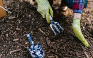 A person wearing gloves using garden tools in soil for planting.