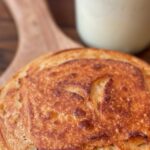Freshly baked sourdough bread on a wooden board with a jar of sourdough starter.